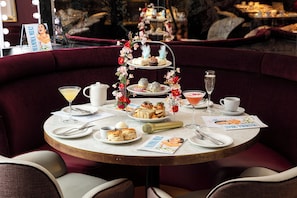 Une table ronde avec un présentoir à gâteaux à plusieurs niveaux, des assiettes de nourriture et un magazine.