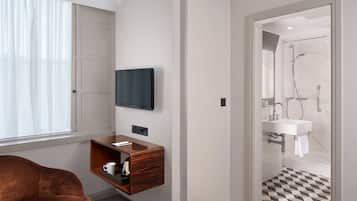 Un baño moderno con ducha, televisor montado y tocador de madera con una taza.