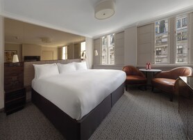 A hotel room with a large bed, a sitting area with a table and chairs, a television, and a window with a city view.