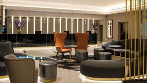 A modern lobby with leather chairs, a sofa, and round tables. There are decorative vases and a reception desk. - Strand Palace Hotel (London)