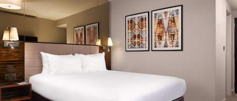 A hotel room with a large bed, a nightstand, a mirror, and two framed pictures on the wall.