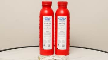 Deux bouteilles rouges étiquetées « Eau non gazeuse » sont posées sur une table blanche, à côté d’une boîte de chocolats.