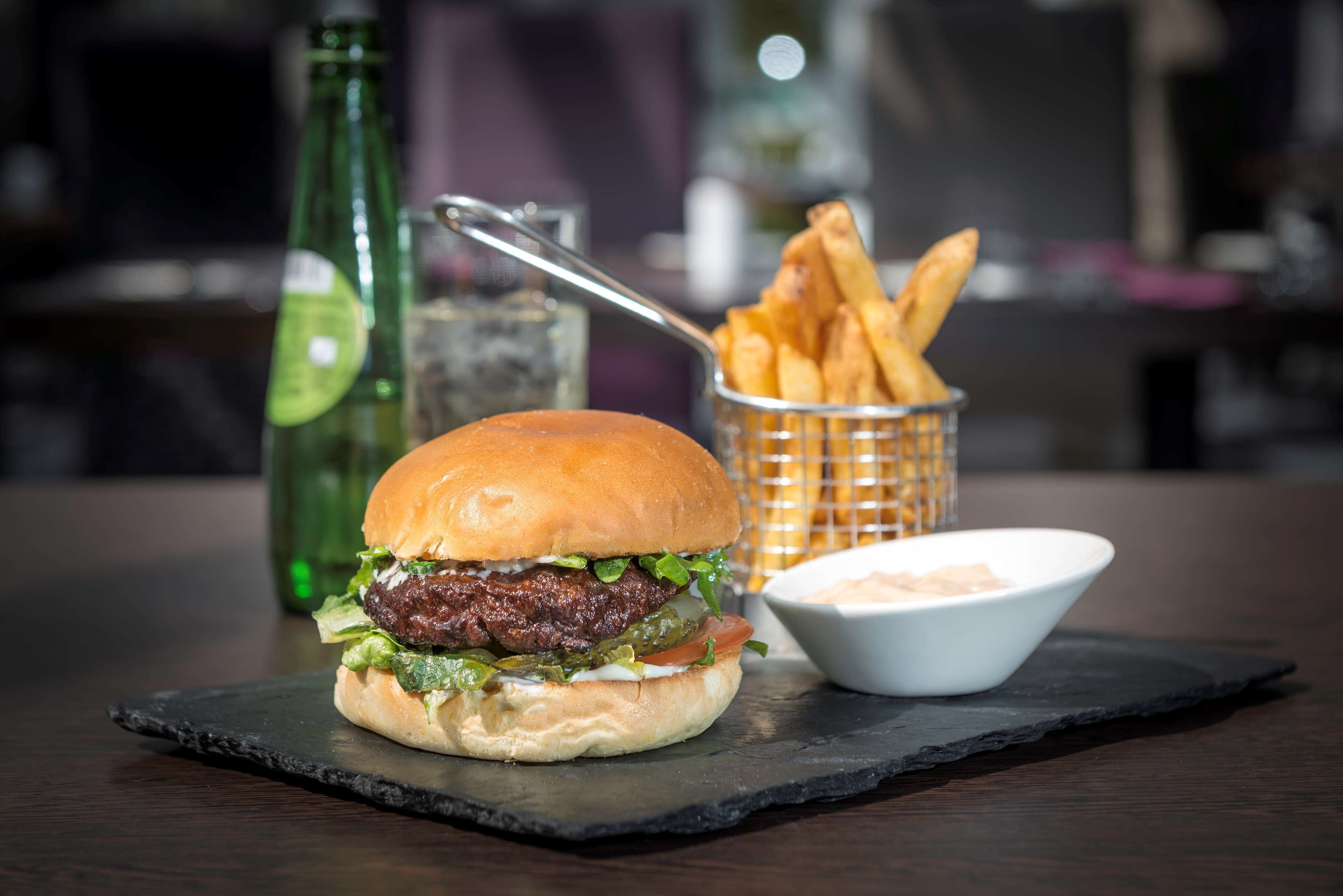 A burger with fries and a dipping sauce on a slate board.