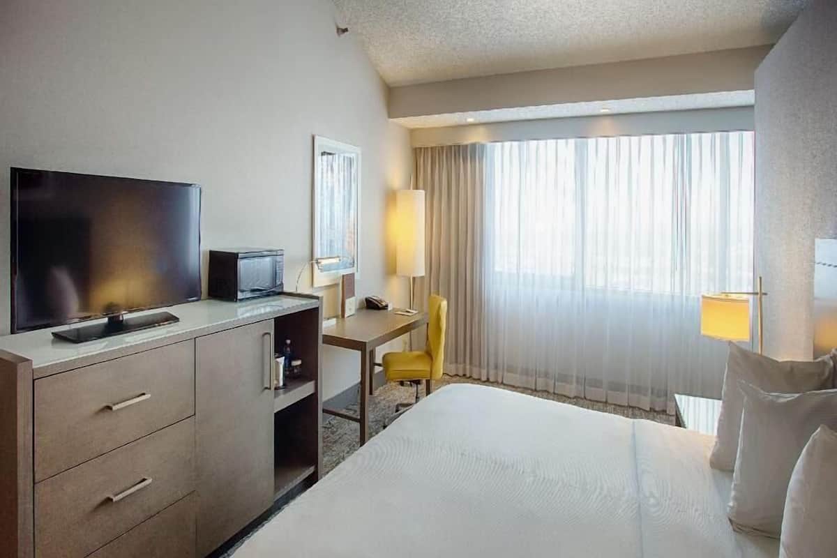 A hotel room with a bed, a desk with a chair, a television, and a window with curtains.