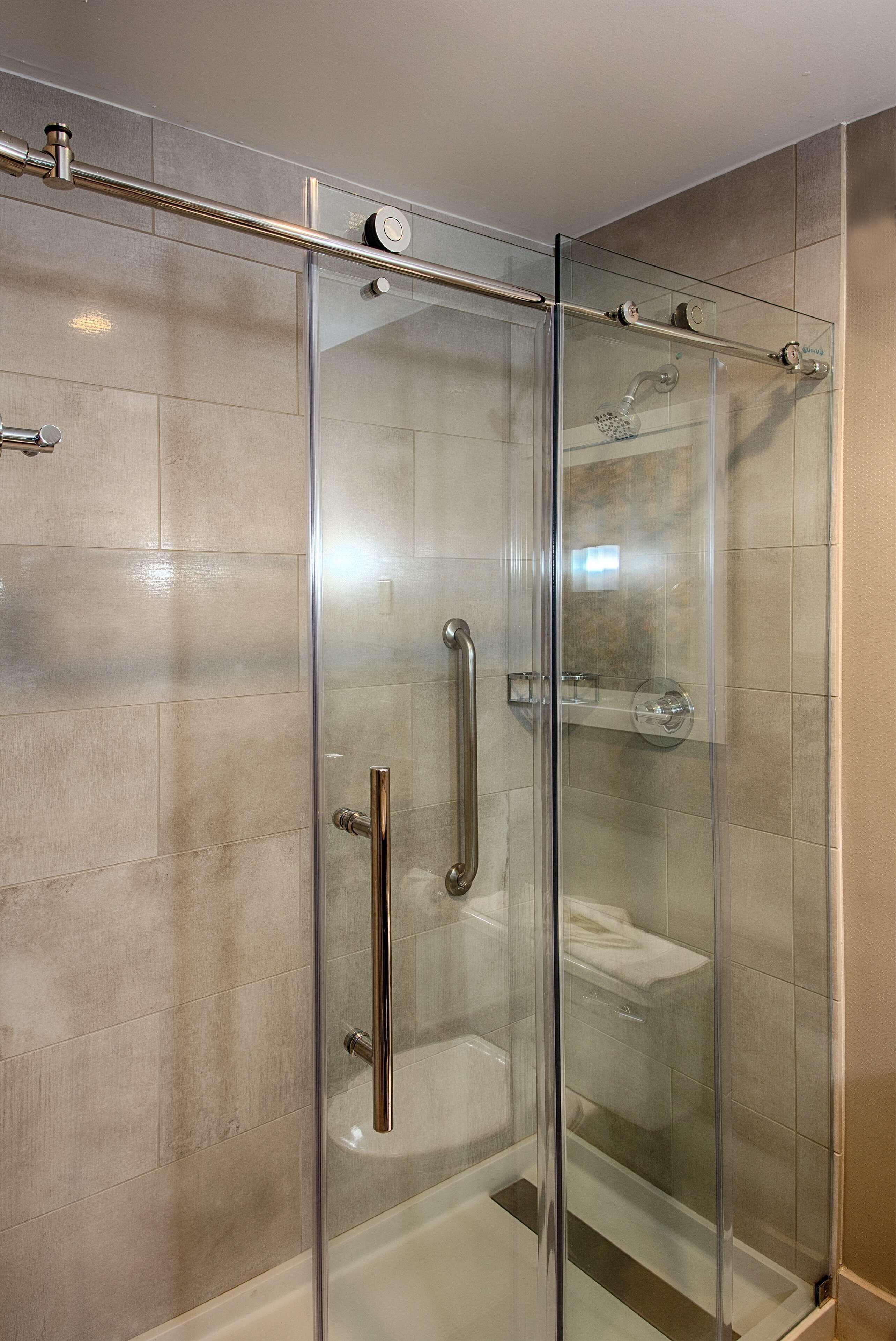 A glass-enclosed shower with a handheld showerhead, a handheld showerhead, and a handheld showerhead.