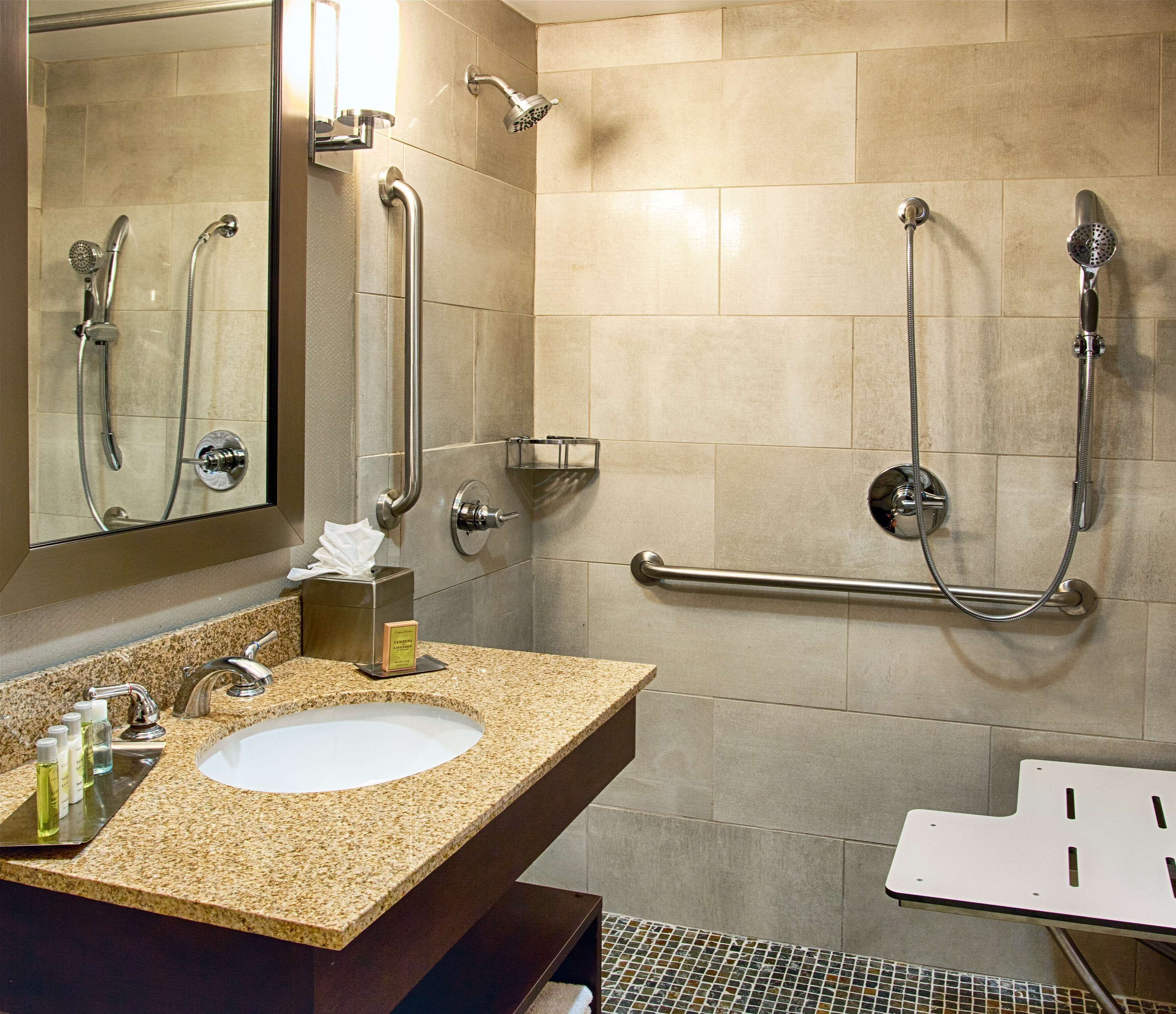 Une salle de bain avec un lavabo doté d’un plan de travail en granit, un miroir, un porte-serviettes et une barre d’appui.