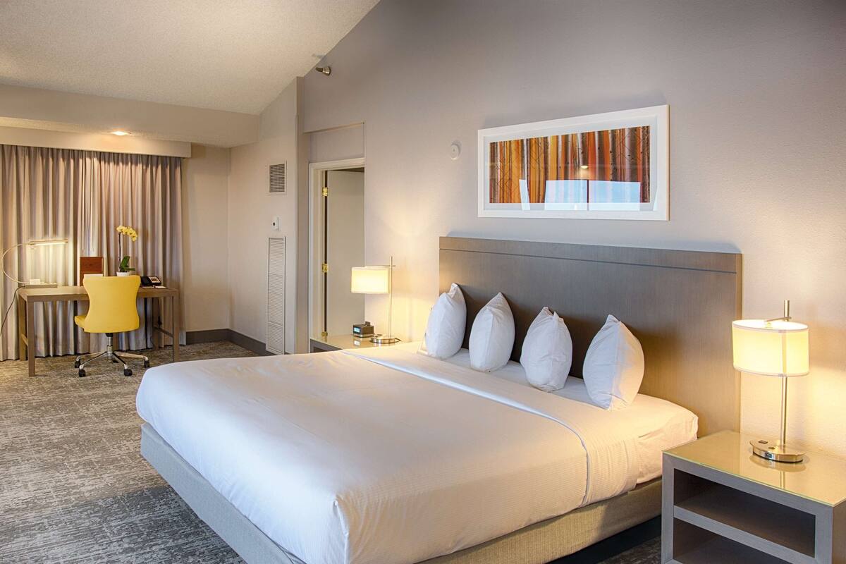 A hotel room with a large bed, a desk with a chair, a lamp, and a painting on the wall.