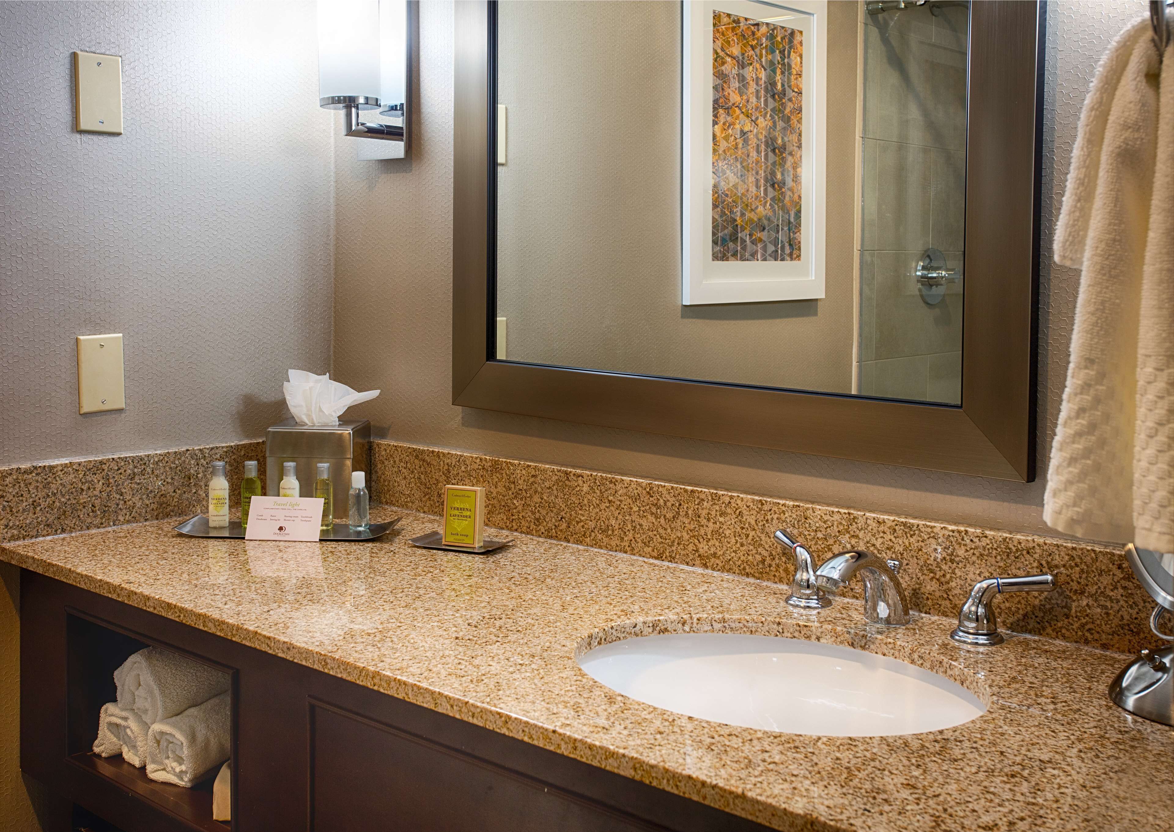 A hotel bathroom with a granite countertop, a white sink, a large mirror, and a towel rack.