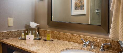 A hotel bathroom with a granite countertop, a white sink, a large mirror, and a towel rack.