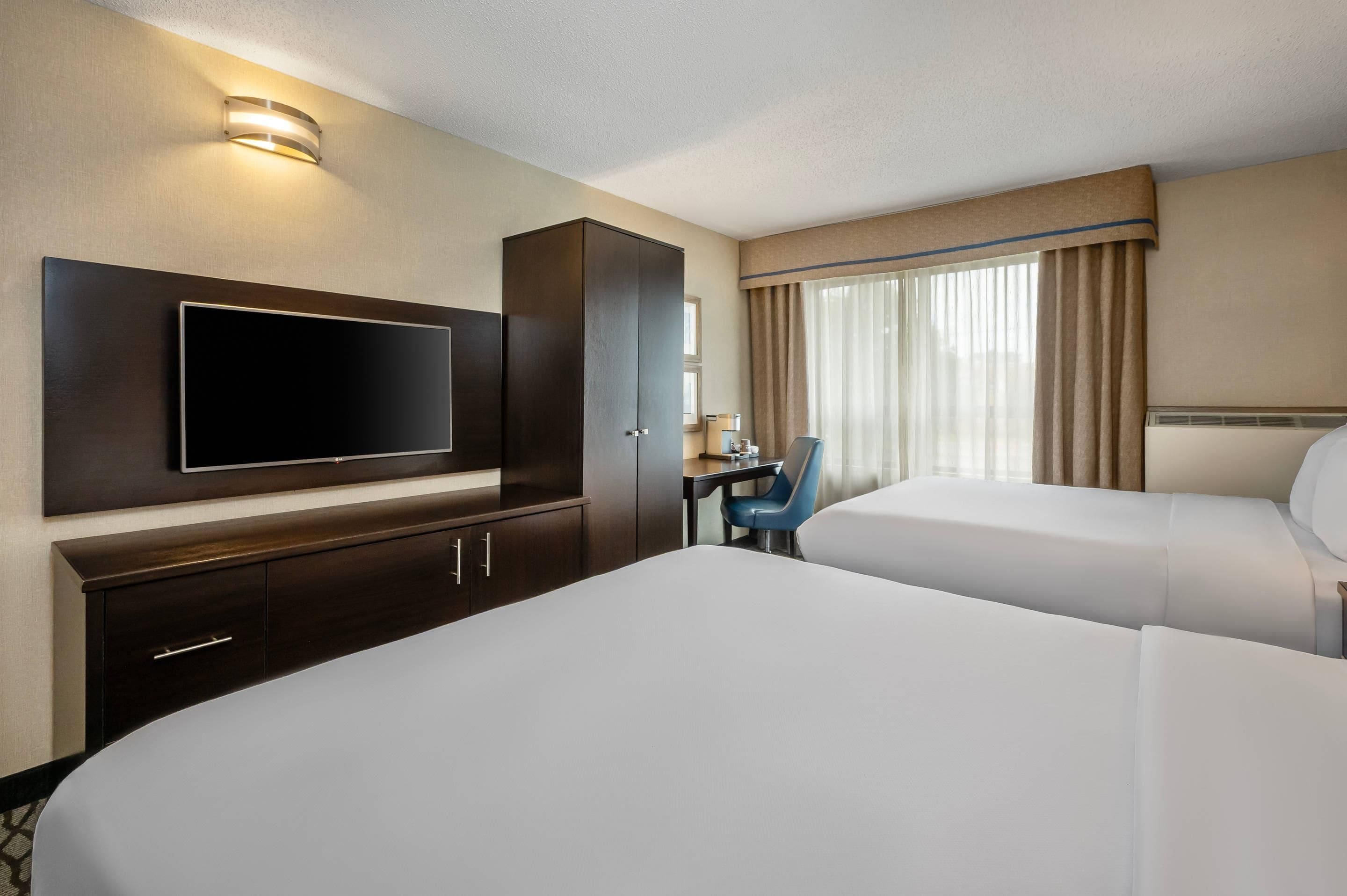 Une chambre d’hôtel équipée d’un grand téléviseur à écran plat, d’un bureau avec une chaise et de deux lits.