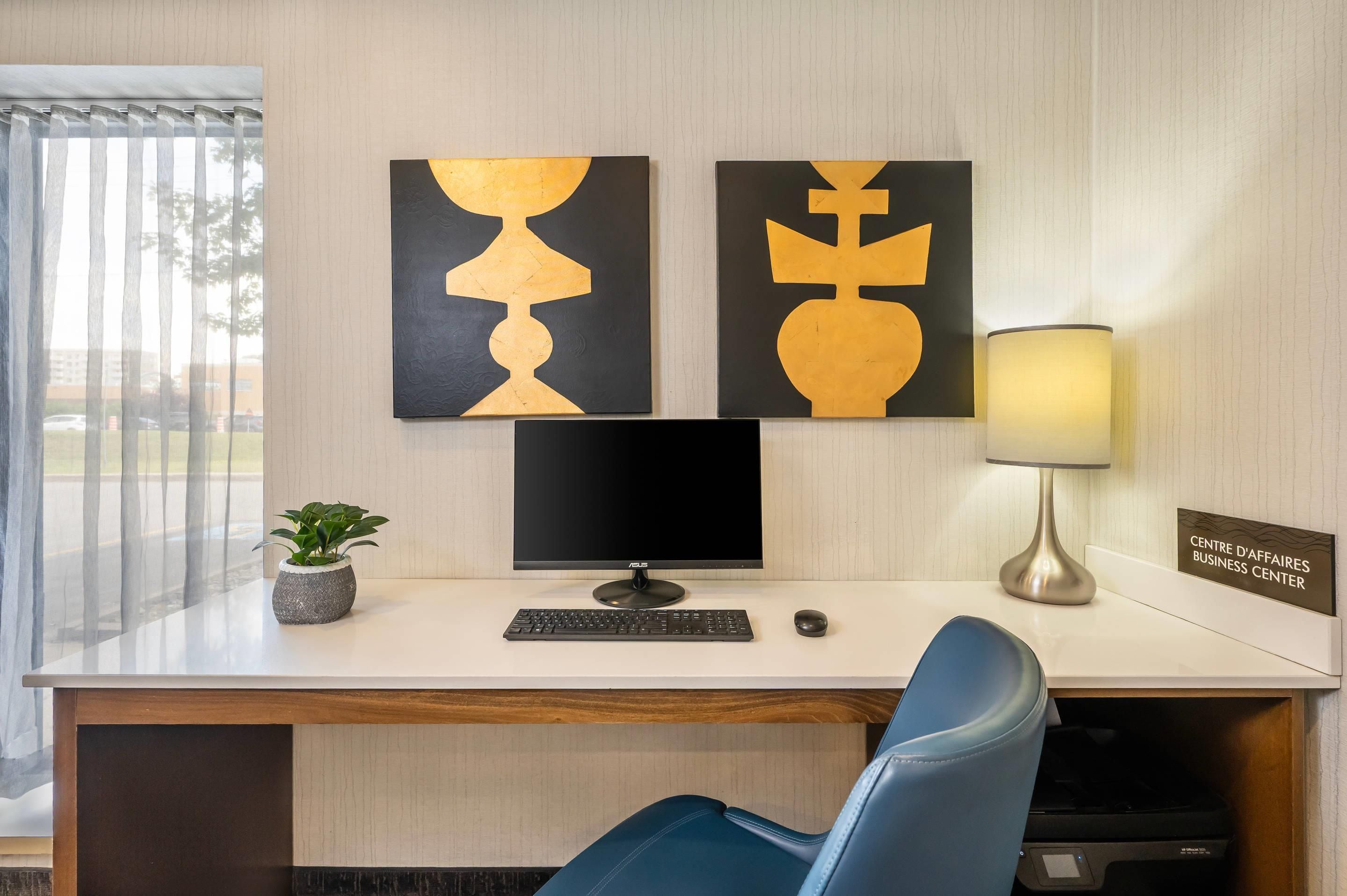 A modern office desk with a computer, keyboard, and mouse, a lamp, and two abstract paintings on the wall.