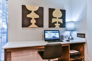 A hotel reception desk with a laptop, a lamp, and a Canon printer. There are two abstract paintings on the wall and a sign that reads "CENTRE D'AFFAIRES BUSINESS CENTER".