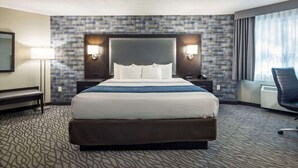 A hotel room with a large bed, a desk, a chair, a lamp, and a view of the outdoors. - Comfort Inn Montréal Aéroport (Pointe Claire)