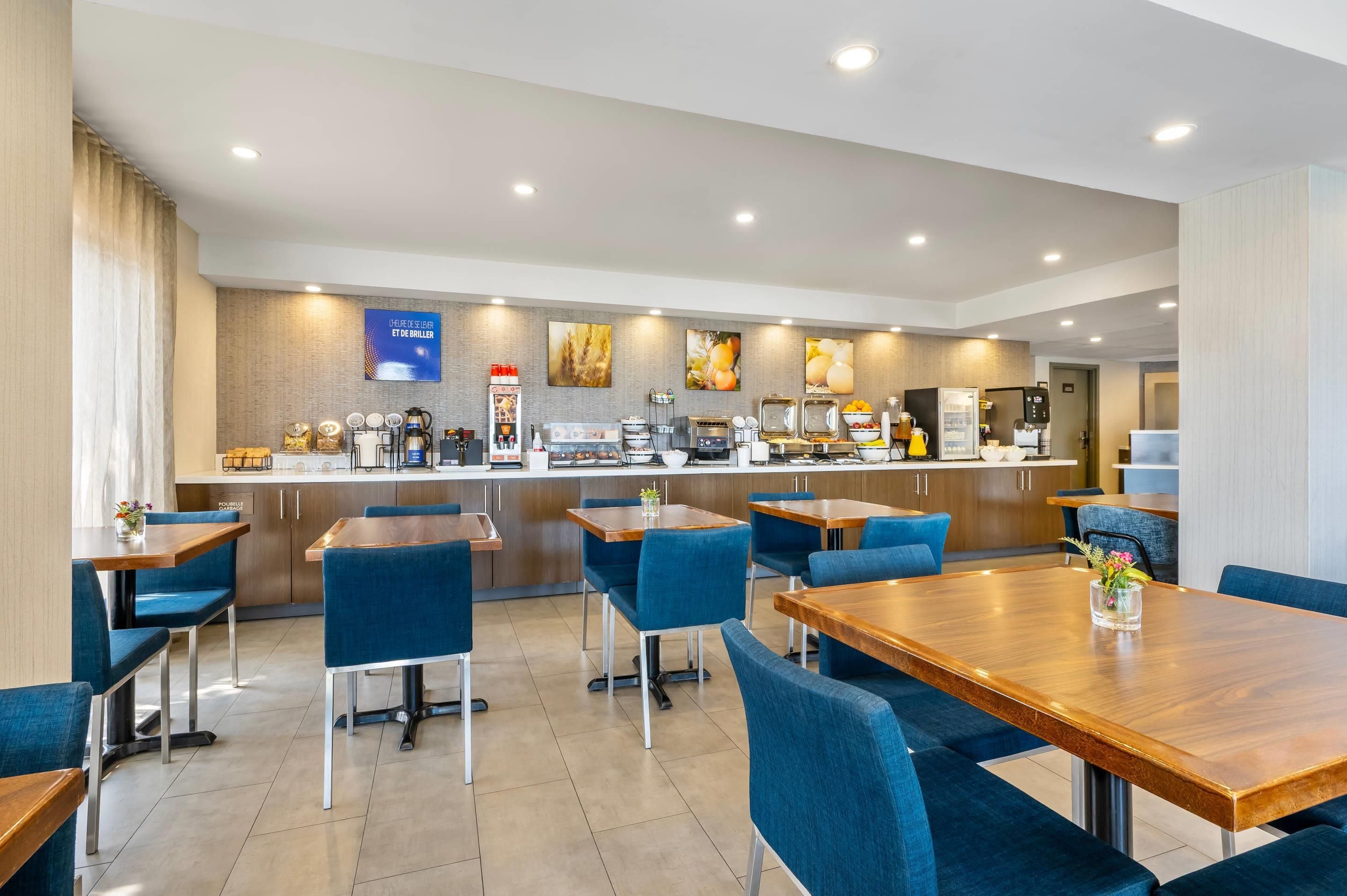 A modern hotel dining area with a buffet setup, blue upholstered chairs, and a wooden table.