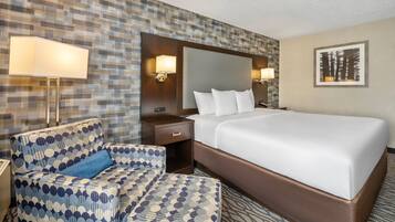 A hotel room with a large bed, a patterned armchair, a nightstand, and two wall-mounted lamps.