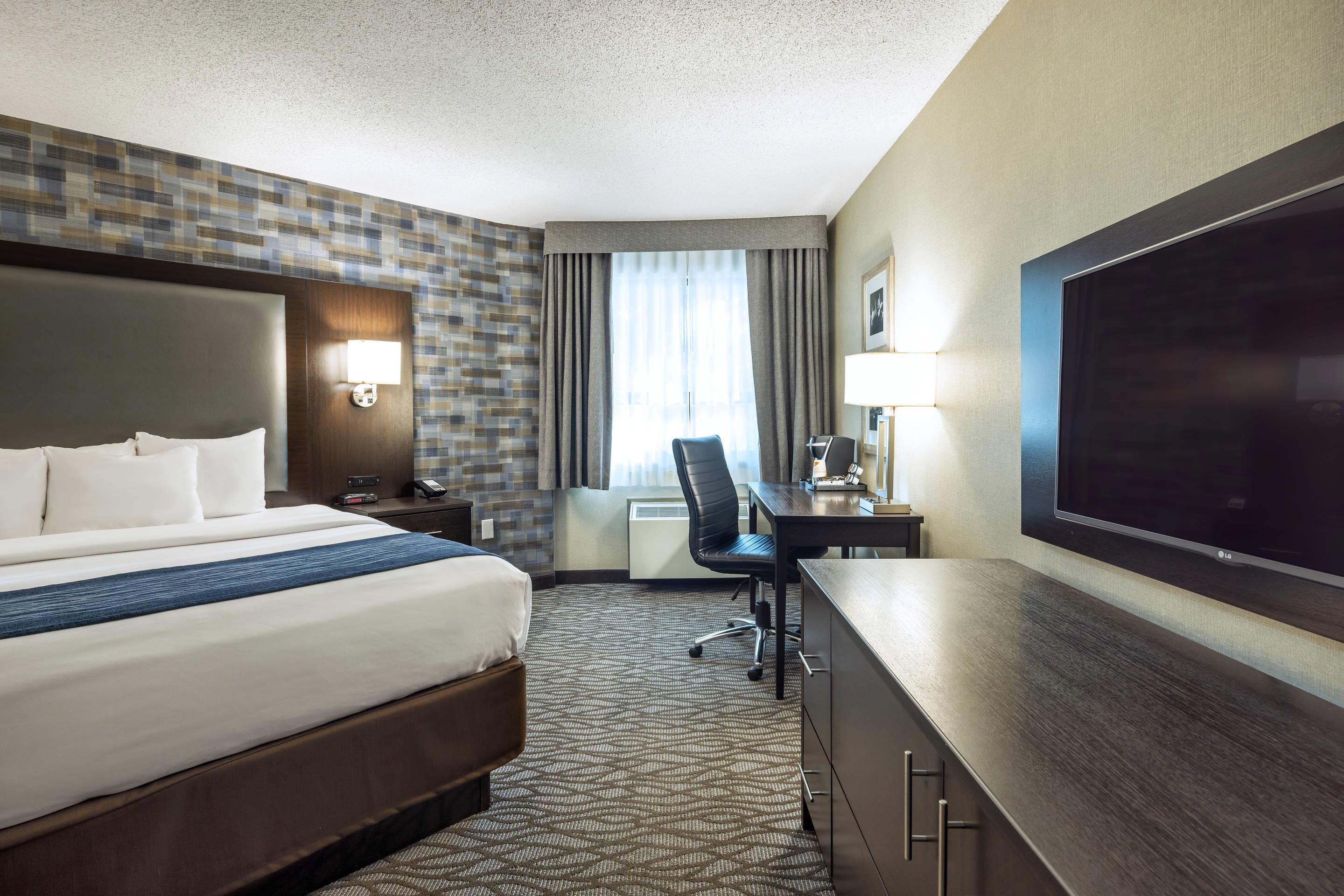 A hotel room with a large bed, a desk, a chair, a TV, and a window with curtains.