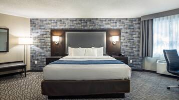 Ein Hotelzimmer mit einem großen Bett, zwei Nachttischen, einem Schreibtisch, einem Stuhl, einem Spiegel und einem Fenster mit Vorhängen.