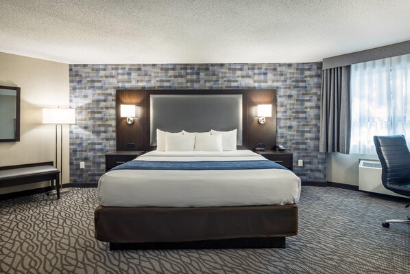 A hotel room with a large bed, two bedside tables, a desk, a chair, a mirror, and a window with curtains.