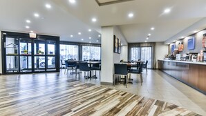 A spacious hotel lobby with a modern design, featuring a wooden floor, a reception desk, and a dining area with tables and chairs. - Comfort Inn Montréal Aéroport (Pointe Claire)