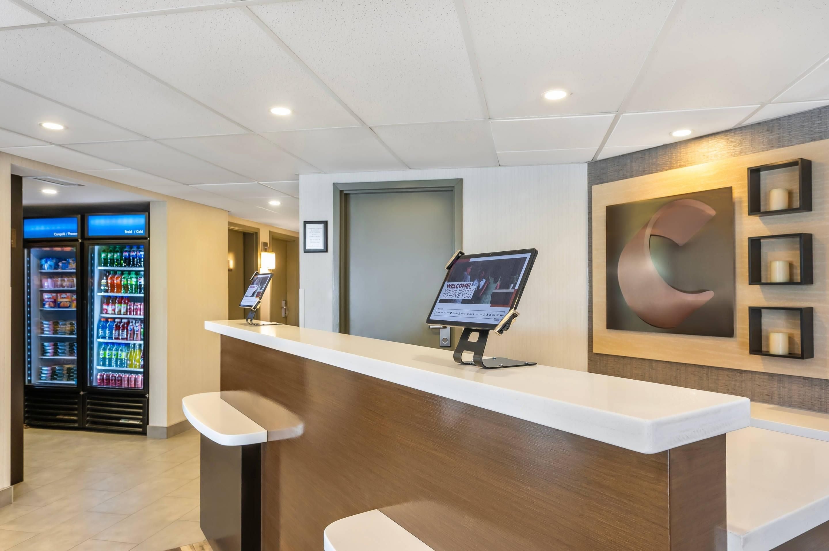 A reception desk with a digital screen, a vending machine, and a wall with a large letter 'C'.