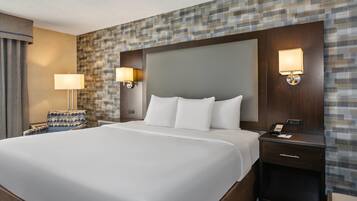 A hotel room with a large bed, two bedside lamps, a nightstand, a patterned wall, and a window with curtains.