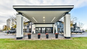 A modern building with a covered entrance, large windows, and potted plants in front. - Comfort Inn Montréal Aéroport (Pointe Claire)