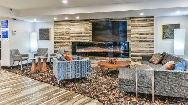 A modern hotel lobby with a fireplace, seating area, and a patterned carpet. - Comfort Inn Montréal Aéroport (Pointe Claire)