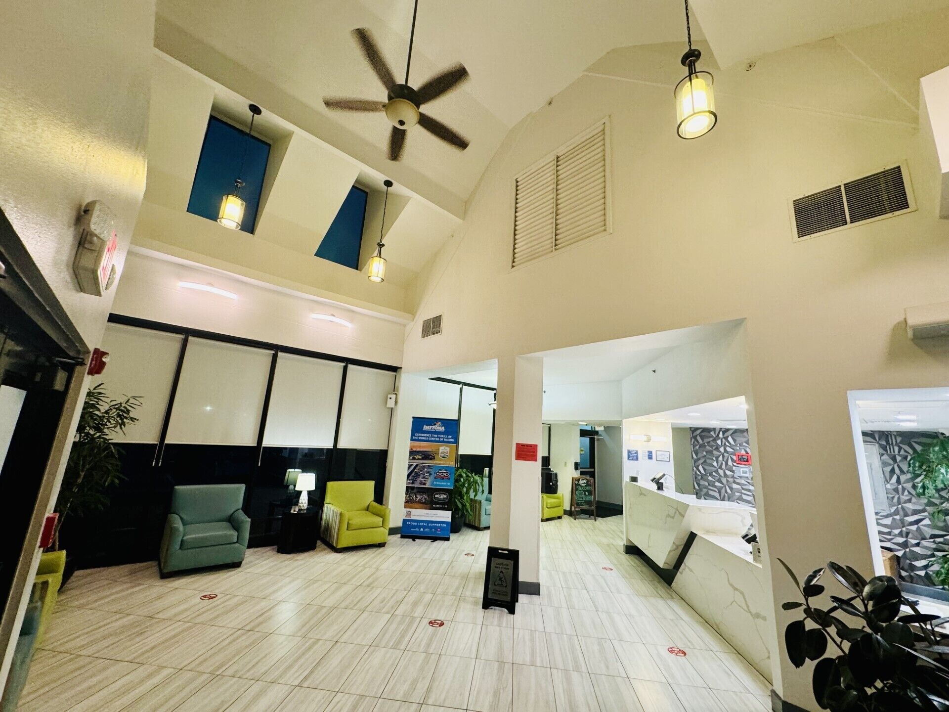 A spacious lobby with a high ceiling, ceiling fans, a reception desk, seating areas, and a large window.