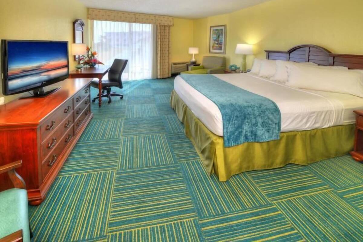 Ein Hotelzimmer mit einem Bett, einem Fernseher, einem Schreibtisch mit Stuhl und einem Vorhangfenster.
