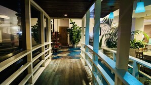 A corridor with a wooden floor, glass railings, and potted plants.