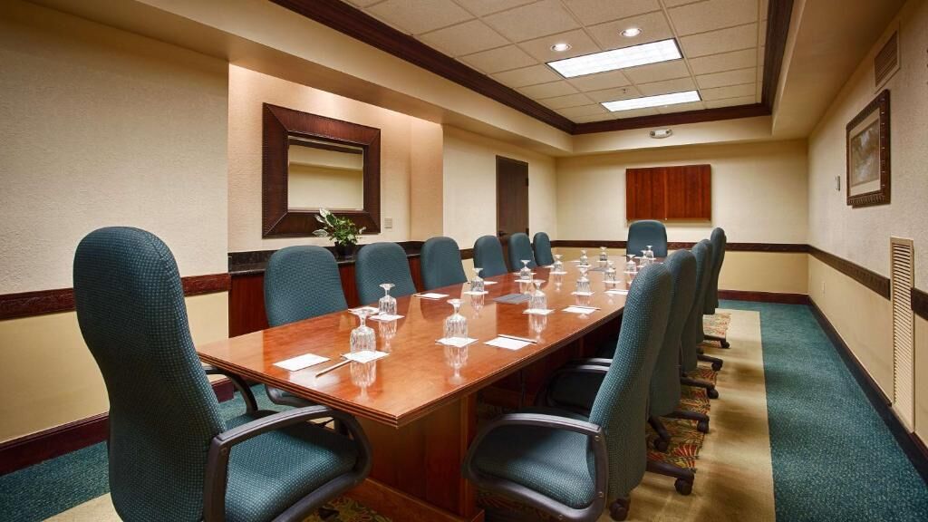A conference room with a long table, multiple chairs, and a large mirror on the wall.