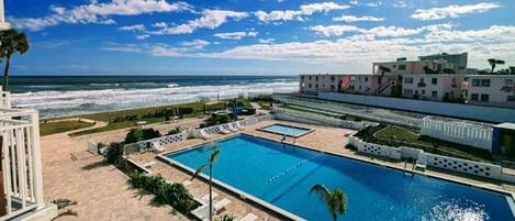 A resort with a large swimming pool, a view of the ocean, and a building with a modern design.