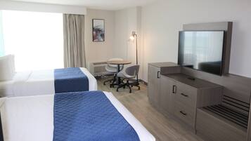 A hotel room with two beds, a desk, a chair, a television, and a lamp.