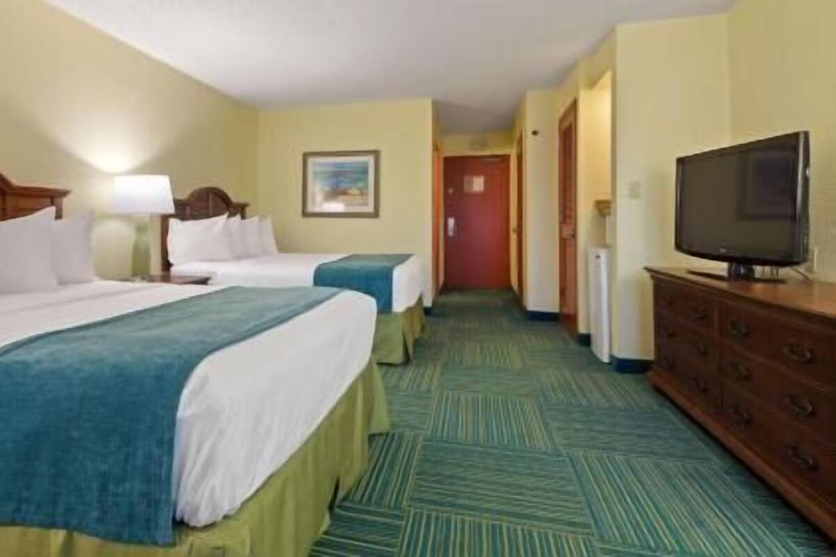 Ein Hotelzimmer mit zwei Betten, einem Fernseher, einem Schminktisch und einem Flur zu einer Tür.
