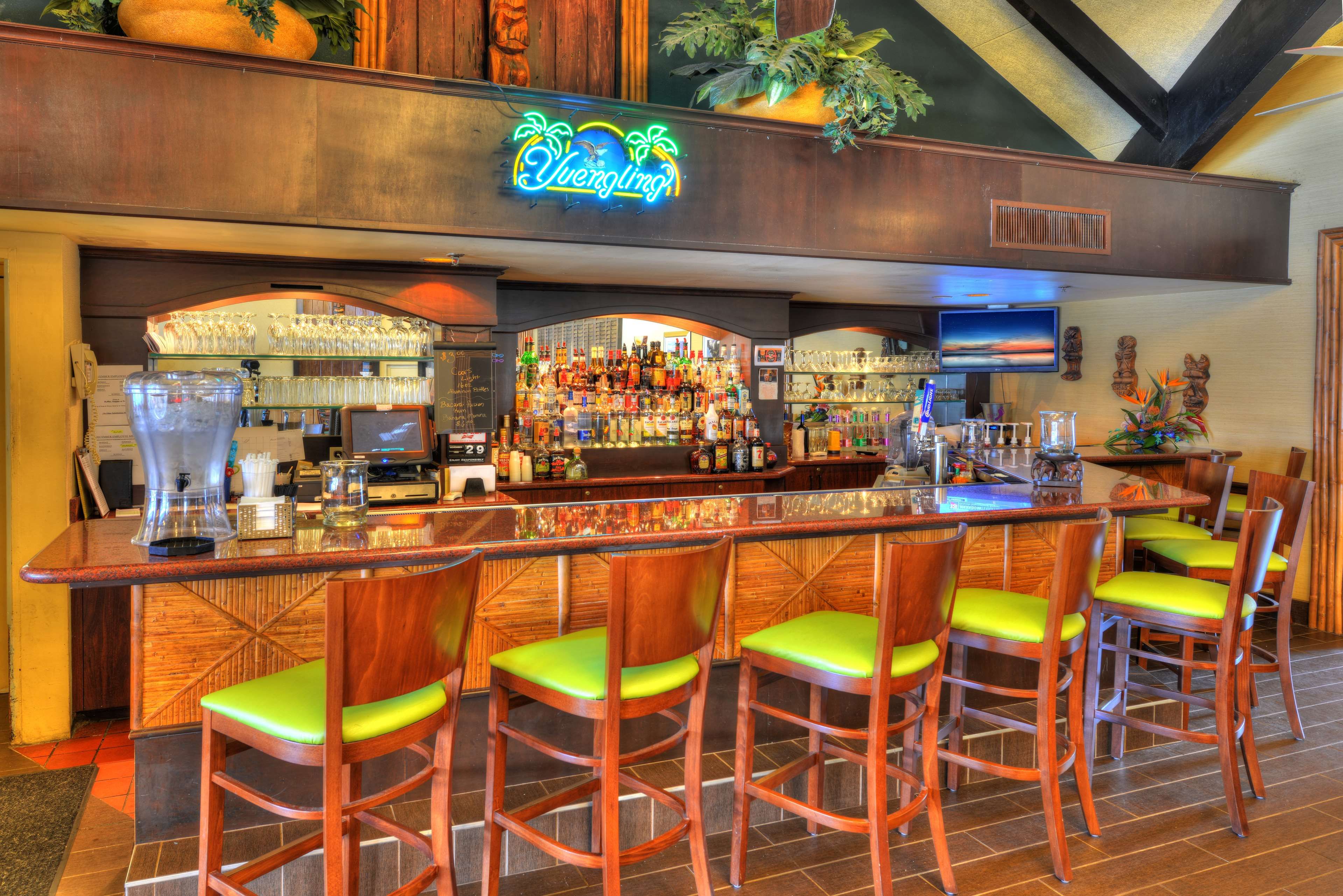 A bar area with a neon sign, a variety of liquor bottles, and bar stools.