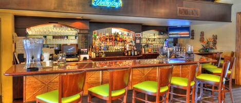 A bar area with a neon sign, a variety of liquor bottles, and bar stools.