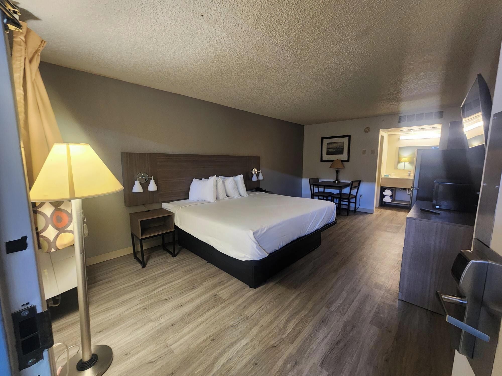 A hotel room with a bed, bedside tables, a desk with a chair, a TV, and a kitchenette.