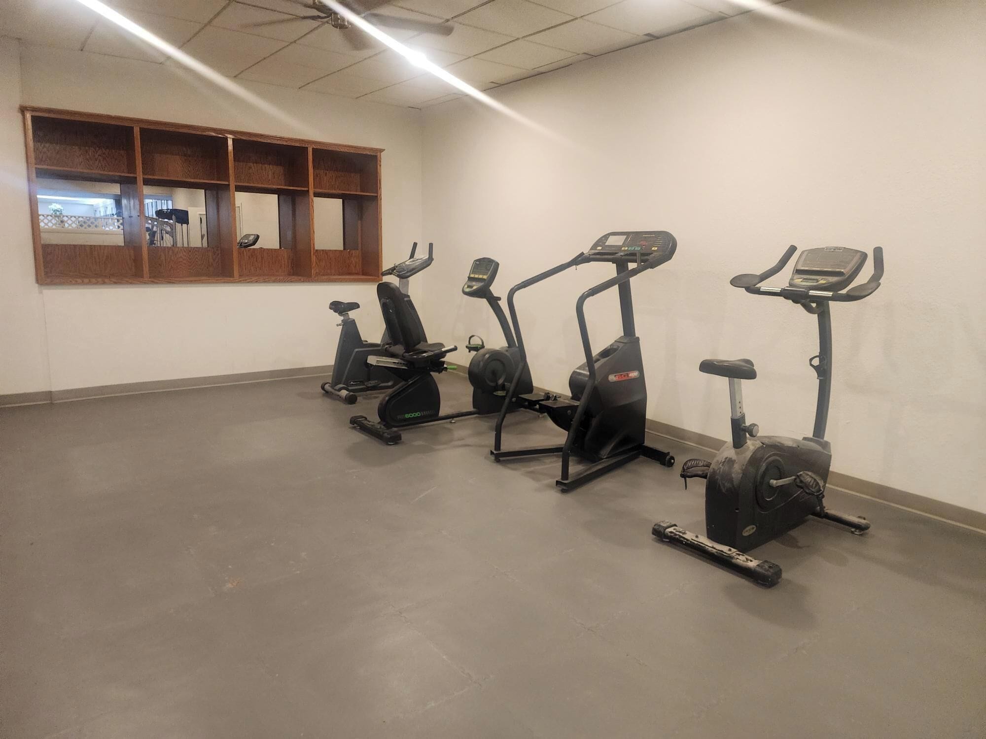 Un gimnasio con cuatro bicicletas estáticas, un estante de madera y un amplio ventanal.