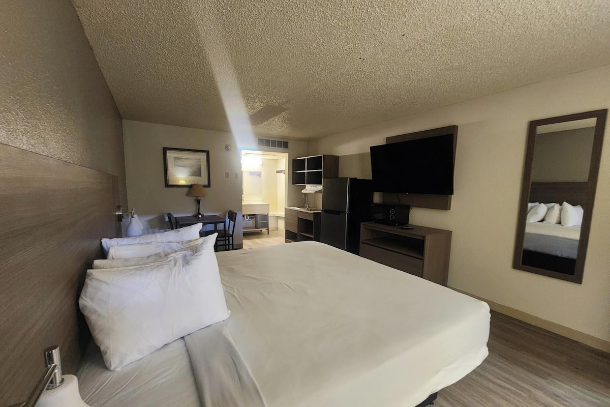 A hotel room with a large bed, a desk, a chair, a TV, and a mirror.
