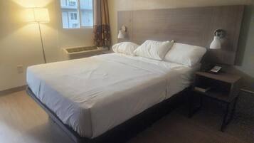 A hotel room with a large bed, two bedside lamps, a nightstand with a phone, and a window with curtains.