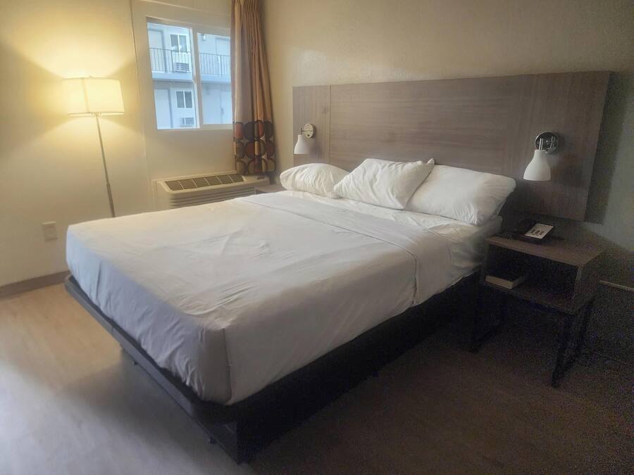 A hotel room with a large bed, two bedside lamps, a nightstand with a phone, and a window with curtains.