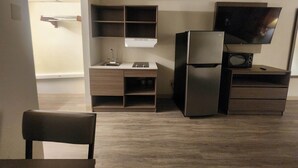 Een kleine keuken met een koelkast, magnetron en een aan de muur bevestigde televisie.