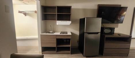 A compact kitchen with a refrigerator, microwave, and a TV mounted on the wall.