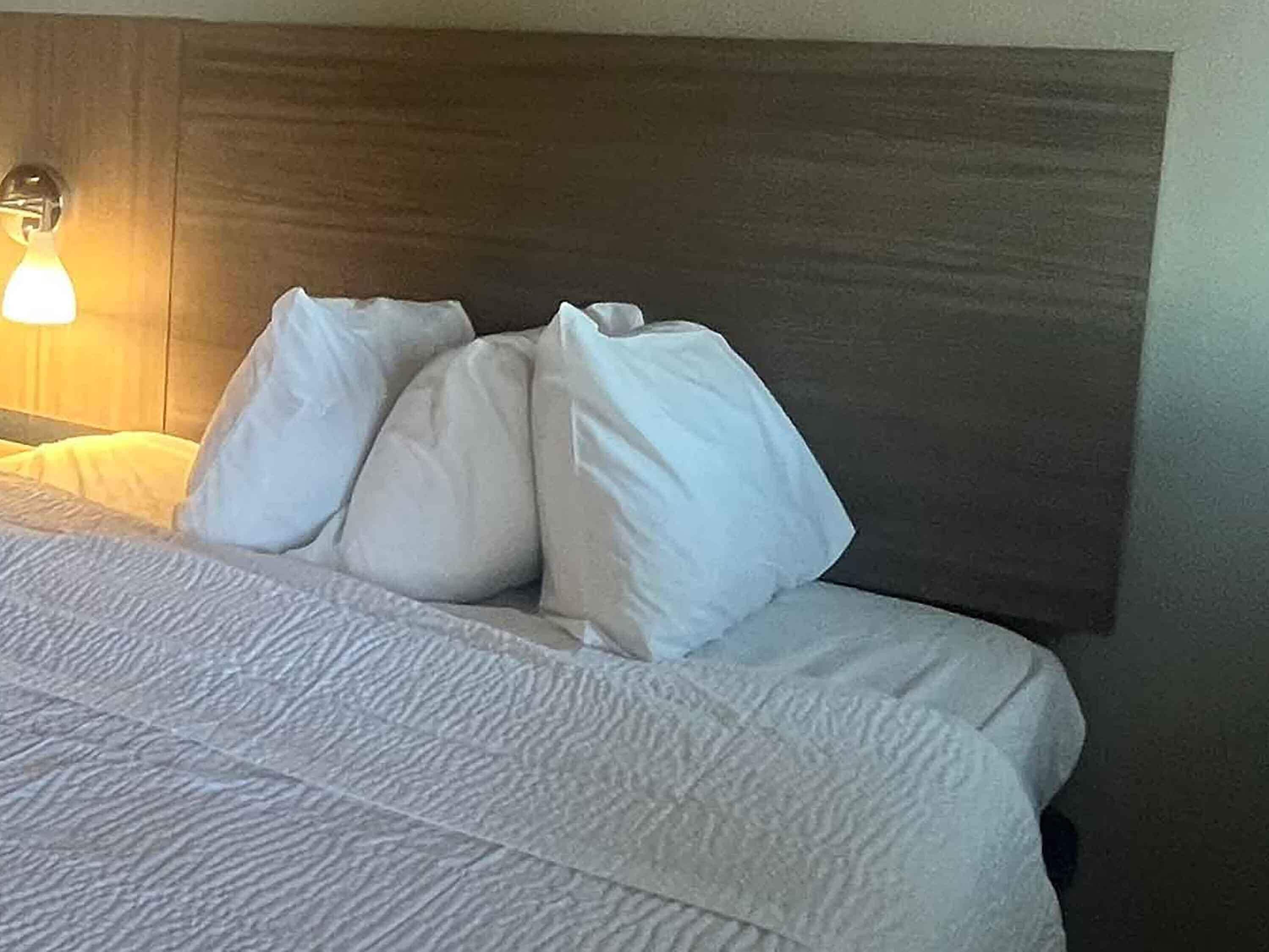 A neatly made bed with white bedding and pillows, a wooden headboard, and a bedside lamp.