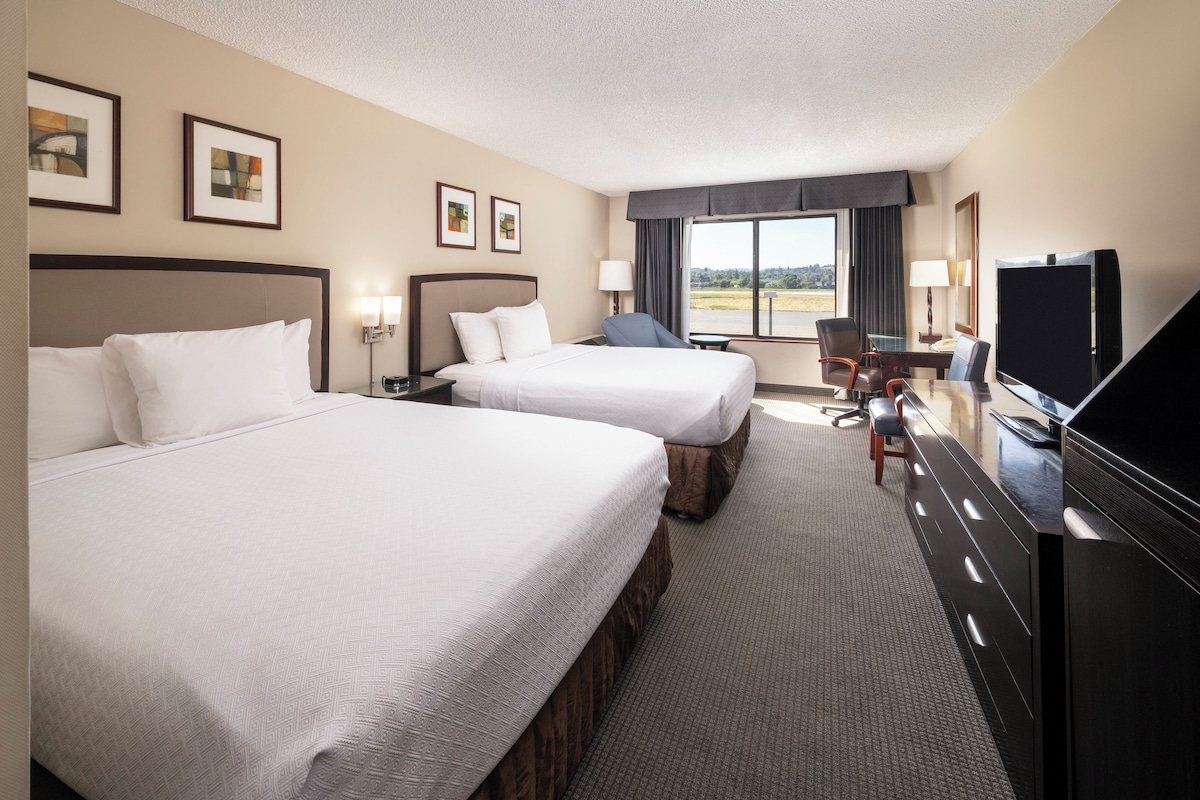 A hotel room with two beds, a desk, a television, and a window with a view.