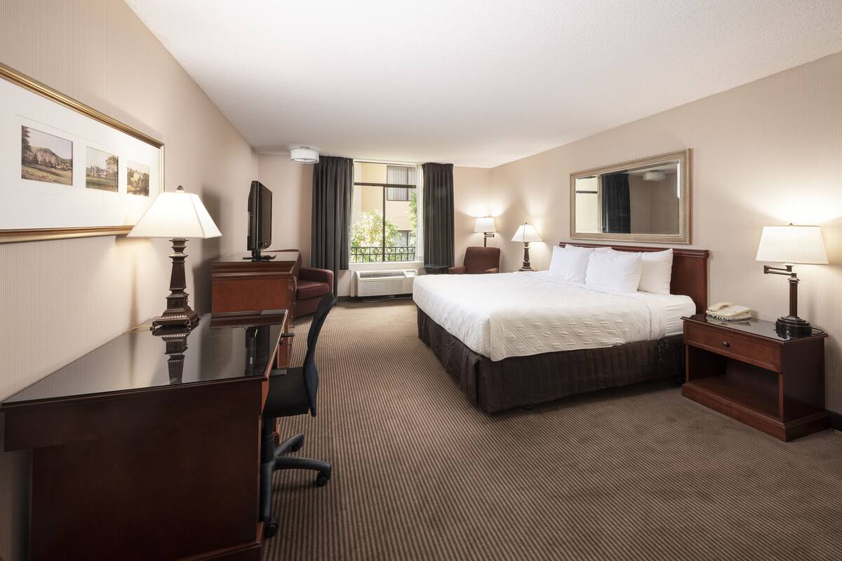 A hotel room with a bed, desk, chair, lamps, and a large mirror.