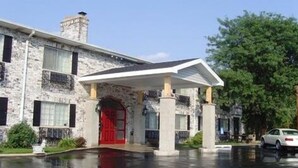 Un edificio de piedra con una puerta roja, un vestíbulo cubierto y un coche blanco estacionado cerca.