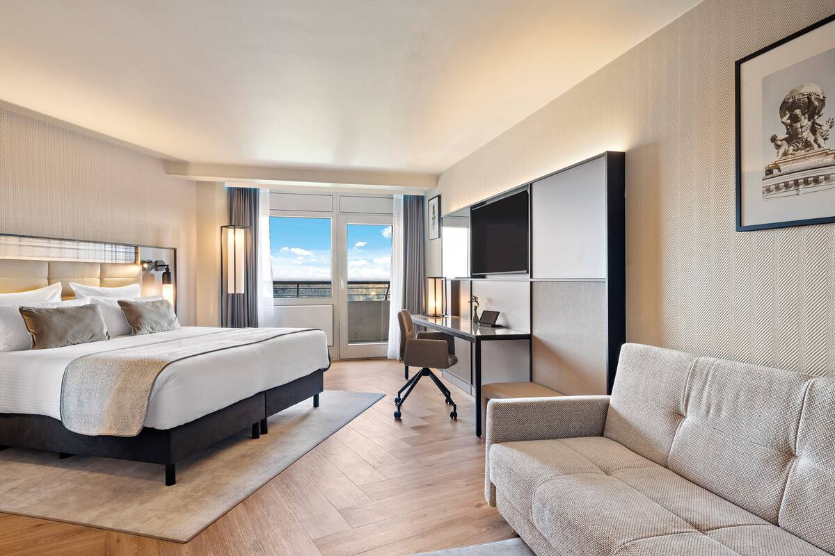 Hotelkamer met een bed, bureau, bank en een groot raam met uitzicht.