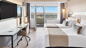 Hotelkamer met een grote televisie, een bureau met stoel, twee bedden en een balkon met uitzicht over de stad.