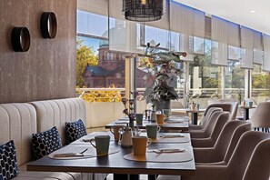 Ein Restaurant mit einem langen Tisch, gepolsterten Sitzgelegenheiten und einem großen Fenster mit Blick auf ein Gebäude und Bäume.